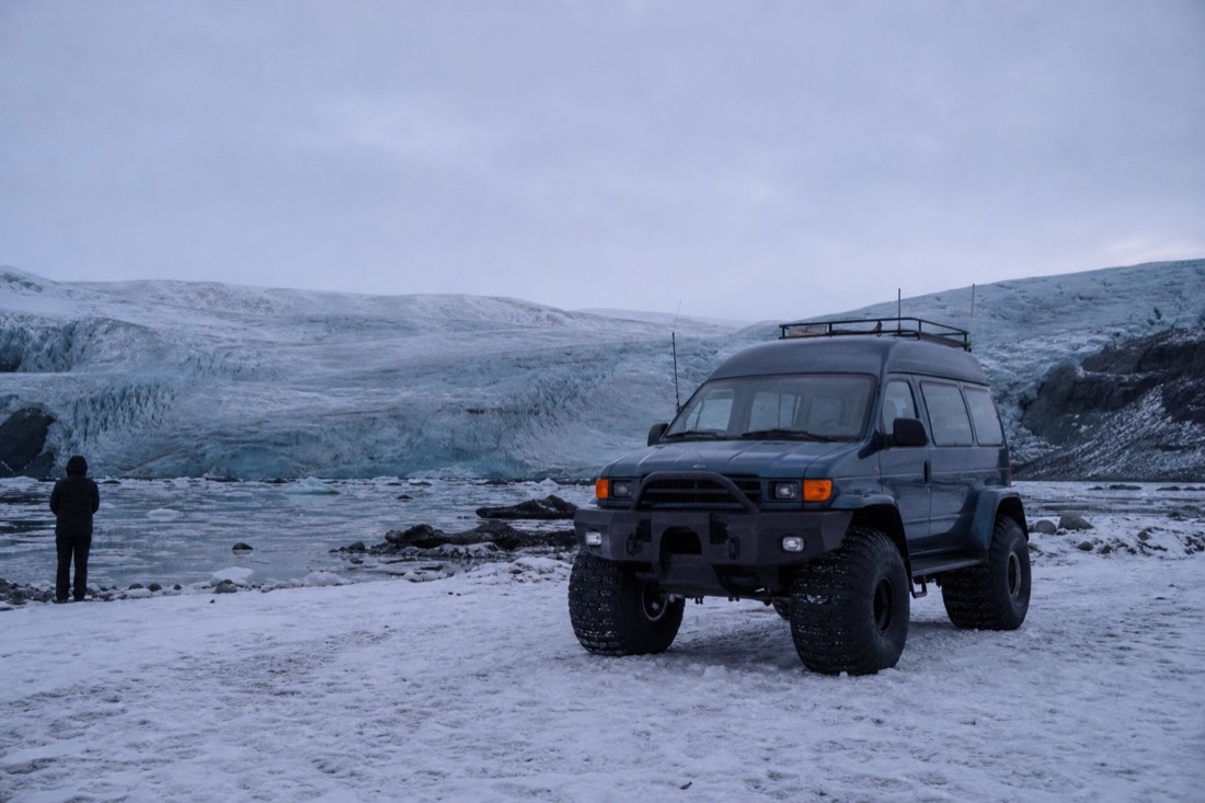 Modified glacier truck on huge tyres parked on snow at a glacier tongue, overcast flat light
