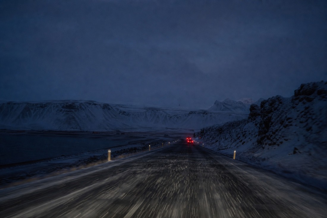 Long dark ring road at night, headlights lighting falling snow, taillights far ahead