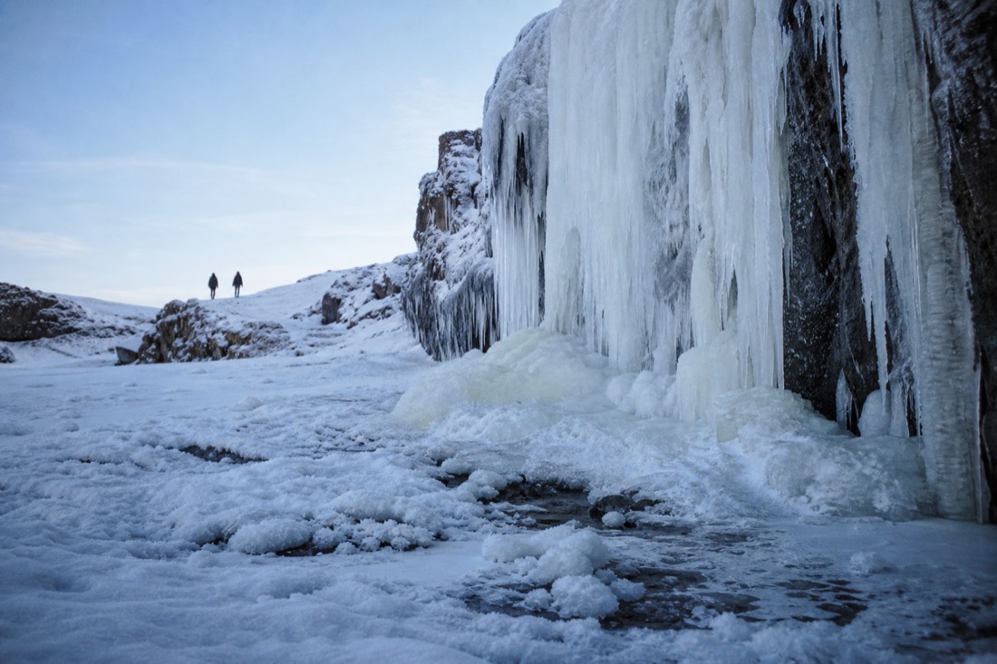 Frozen South Coast waterfall with two distant figures on the path, clear cold blue-hour light