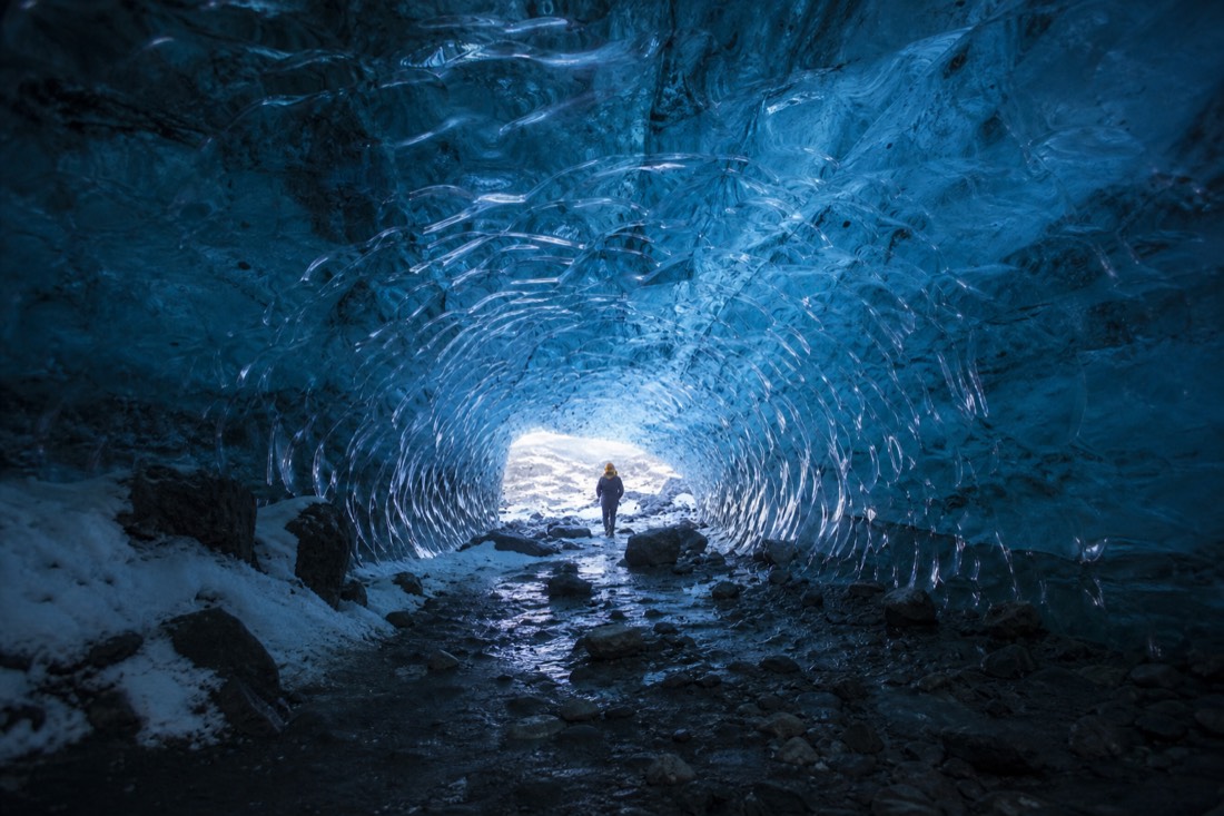 Blue ice cave interior under Vatnajokull, ribbed translucent walls, one distant helmeted figure