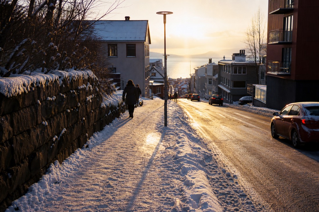 Low golden midday sun skimming a snowy Reykjavik street, long blue shadows across the pavement