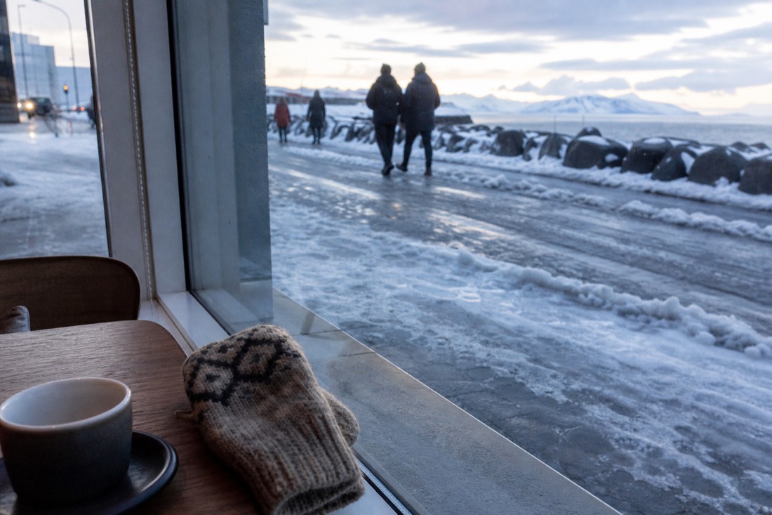Interior window light on a Reykjavik cafe table, snowy street outside, coffee cup and mittens