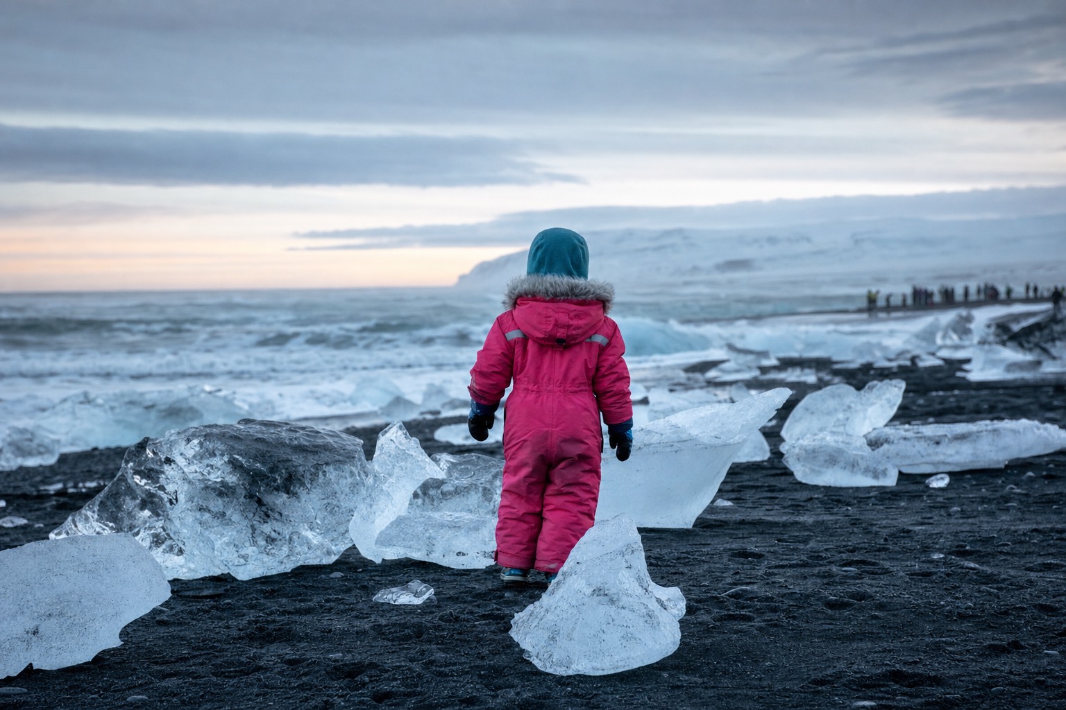 Child in a bright waterproof snowsuit standing on an Icelandic black sand beach in winter light