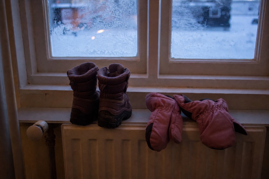 Small child's boots and mittens drying on a radiator beside a frosted window, warm interior light