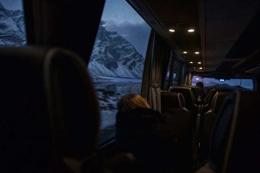 Dark coach interior at night, reading lights on, a small figure asleep against the window