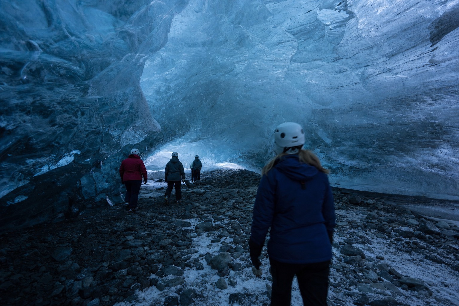 Visitors in helmets standing inside a blue crystal ice cave under Vatnajökull glacier in winter