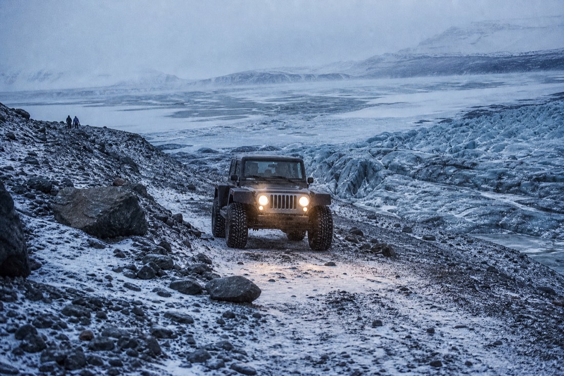 Modified super jeep on a rough moraine track beside the glacier, headlights on in flat grey light