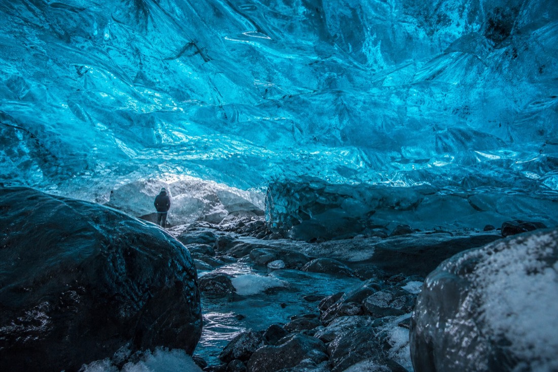 Dense bubble-free glacier ice glowing deep turquoise where daylight filters through a thin roof