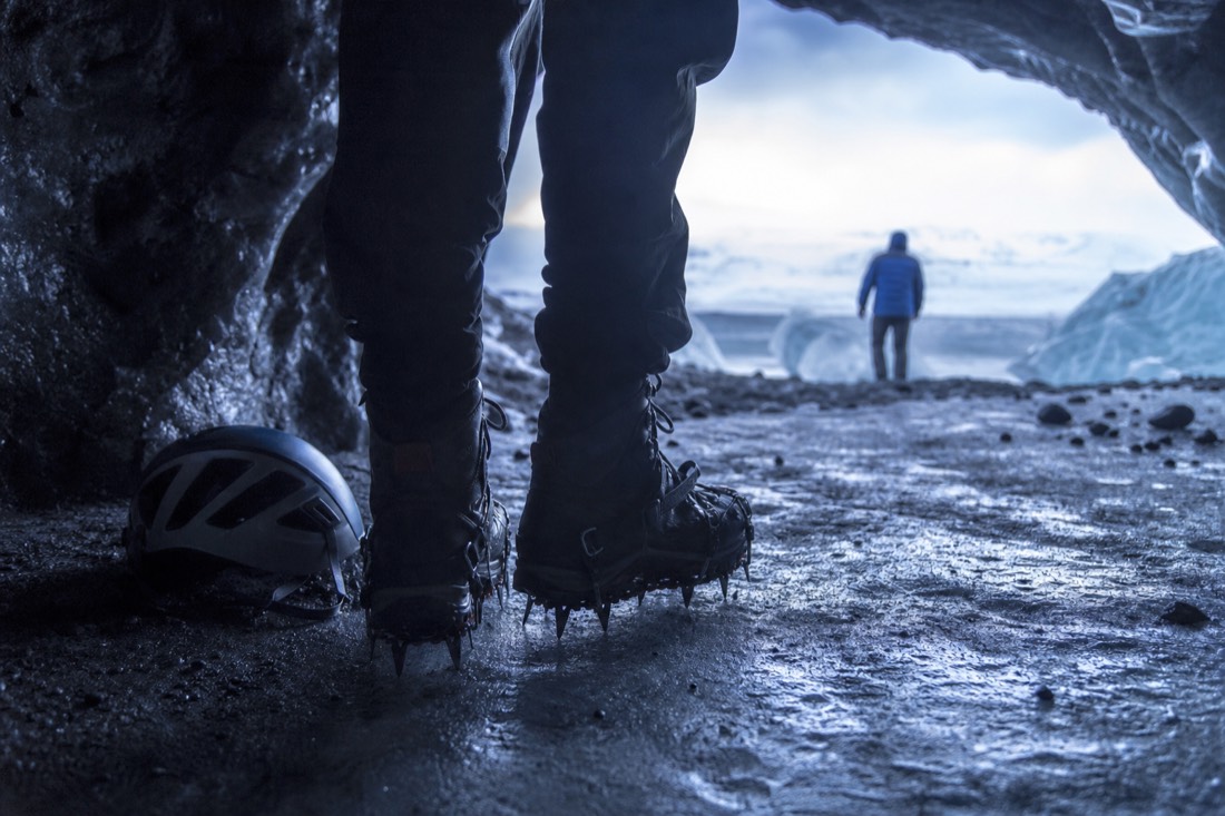Crampons strapped over stiff hiking boots standing on wet gritty cave ice, helmet resting alongside