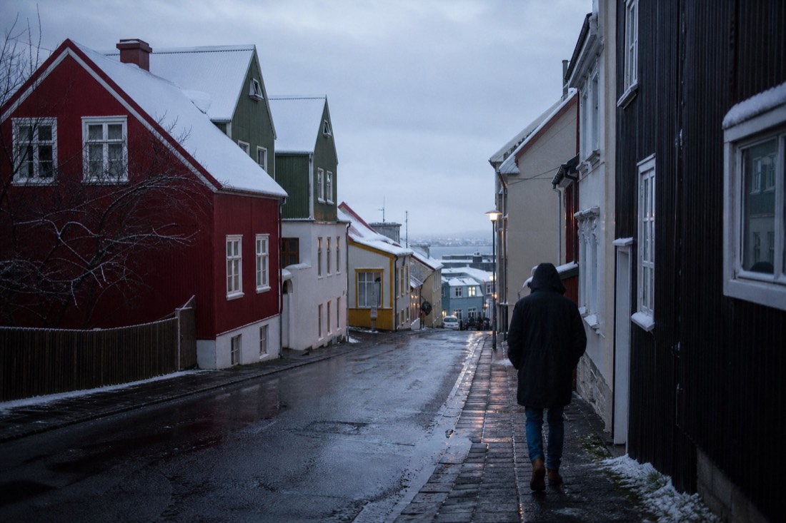 Wet Reykjavik side street of coloured houses under low grey cloud, one walker seen from behind