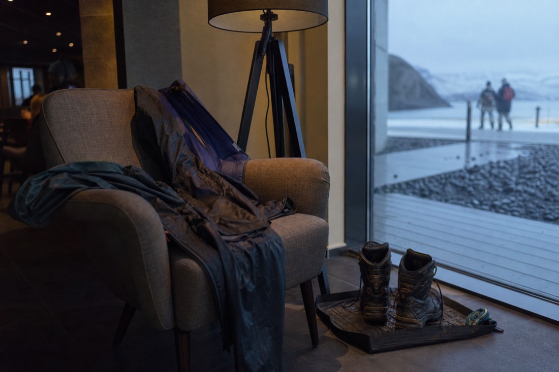 Hotel lobby armchair at dusk with wet waterproofs draped over it and boots drying beside