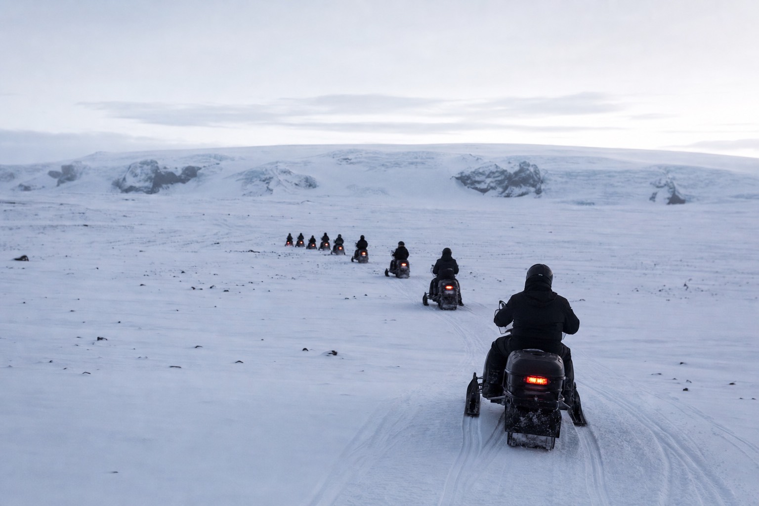 A line of snowmobiles crossing the white surface of Langjökull glacier in flat winter light
