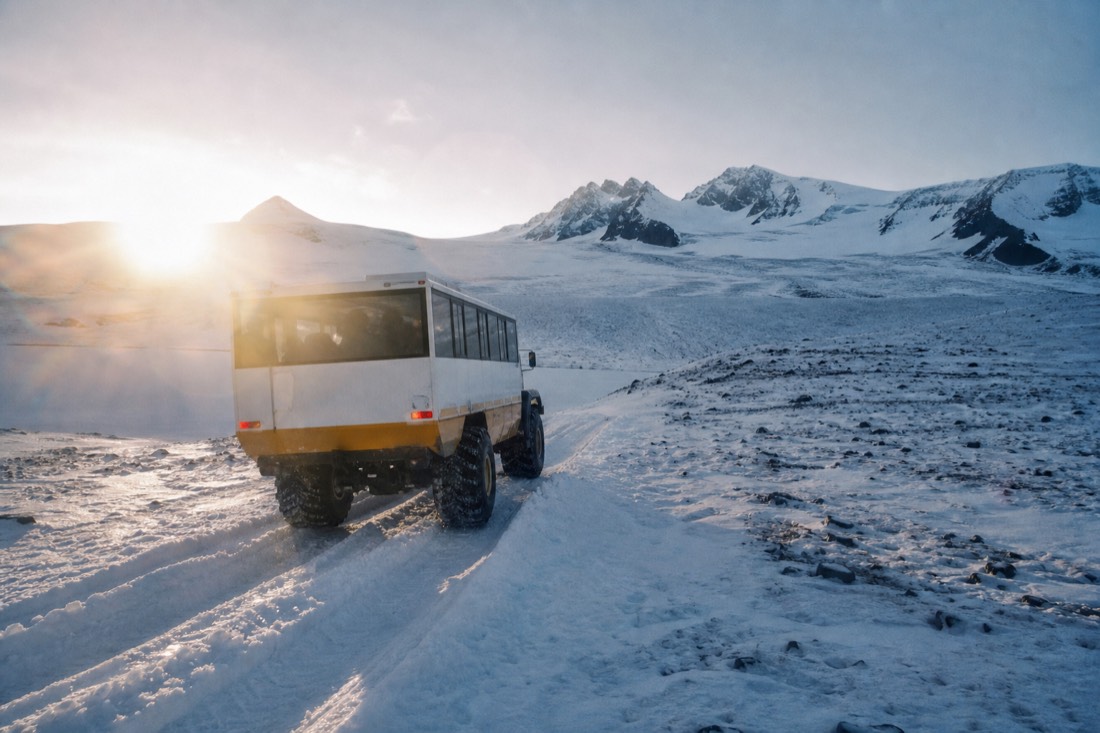 Large-tyred glacier transfer truck climbing a snow track towards the ice cap, low arctic sun