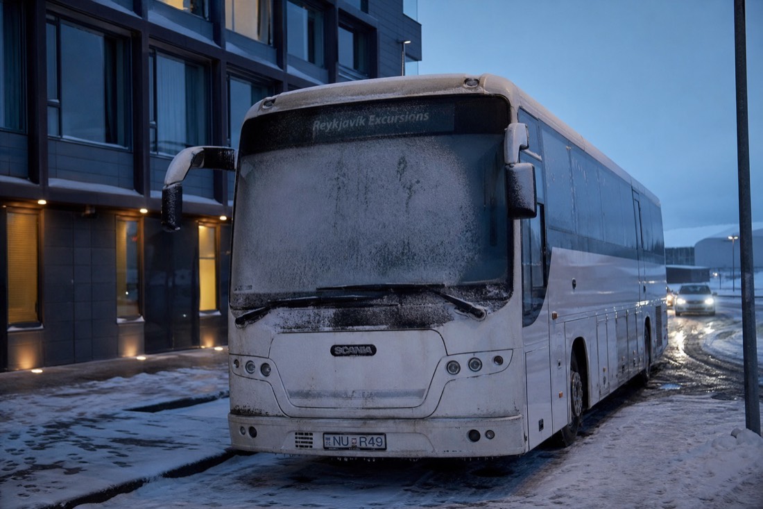 Empty tour coach parked outside a Reykjavik hotel in the dark, windscreen frozen, nobody boarding