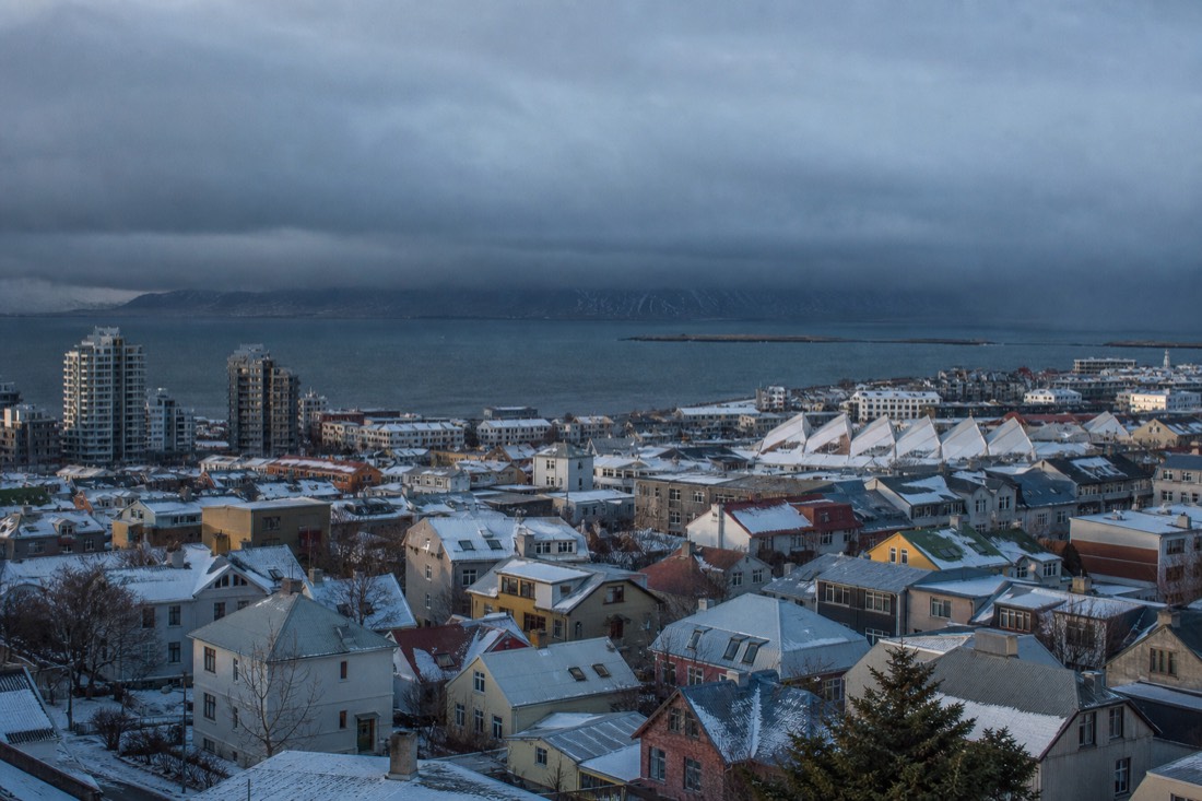 Bright still morning over Reykjavik's coloured rooftops while heavy dark cloud sits on the horizon