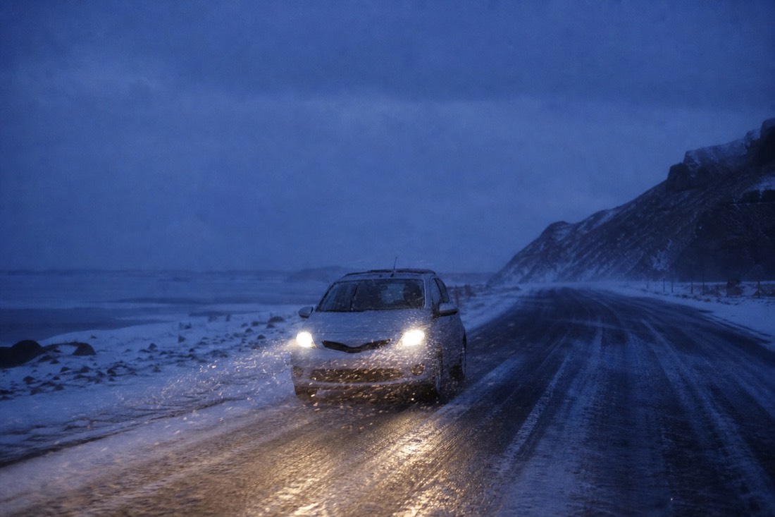 Small hire car on an unlit icy road at night, headlights catching blowing snow