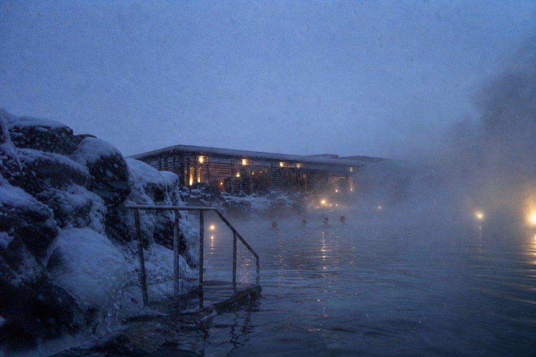 Steam rising off an outdoor geothermal pool in Reykjavik while sleet falls through the dark