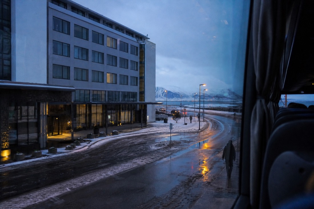 View from a coach window of wet Reykjavik hotel streets at blue hour, lamplight reflected on tarmac