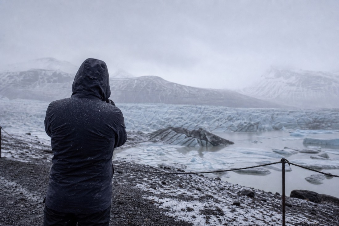 Traveller in waterproofs seen from behind at a snowy roadside viewpoint under flat grey overcast light