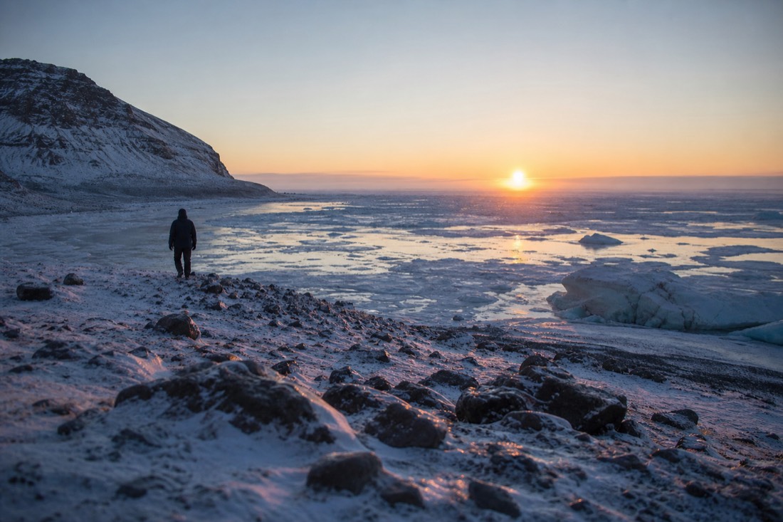 Low orange midday sun barely clearing a white horizon over a frozen Icelandic plain