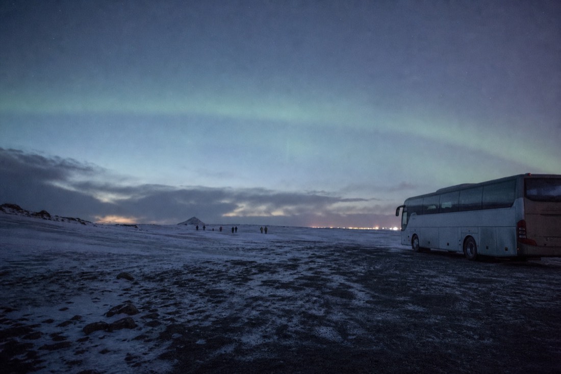 Empty dark field beside a parked coach with a faint pale aurora arch above the skyline