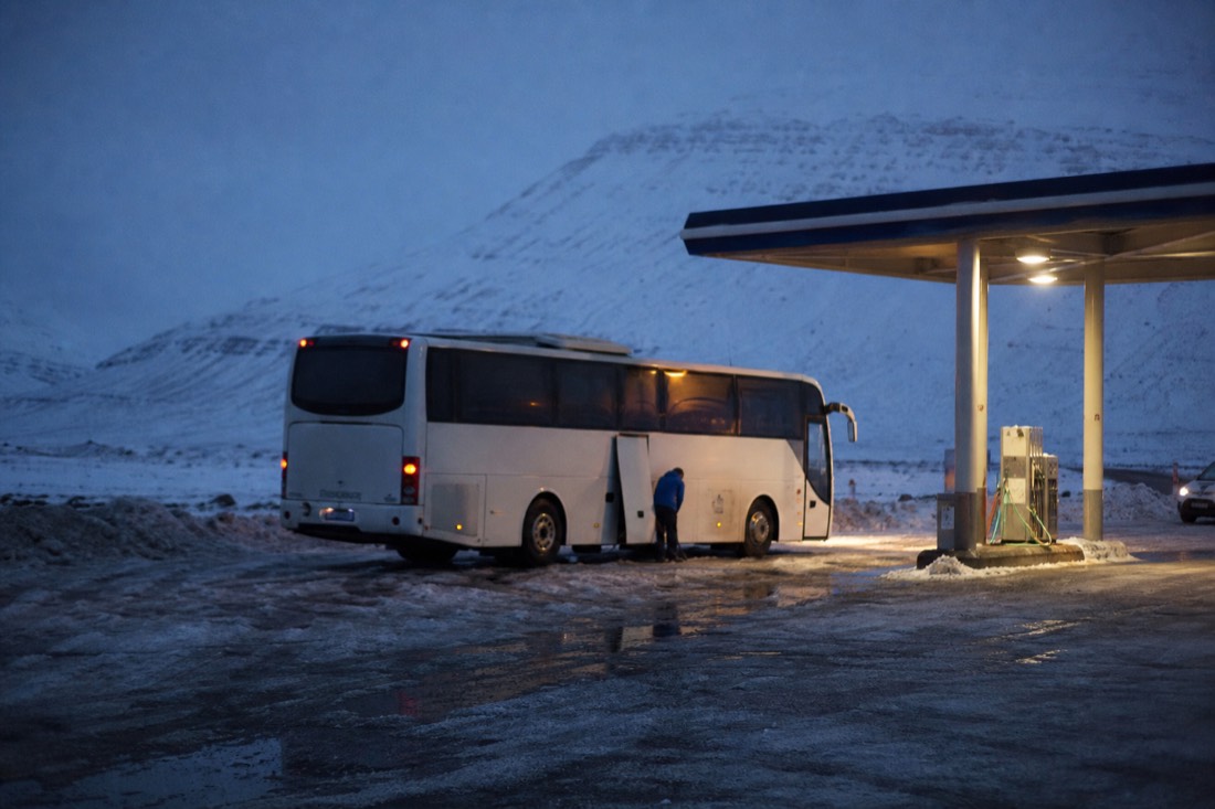 Unbranded petrol station forecourt in the dark, lit pumps, a coach refuelling on packed snow
