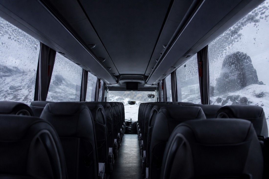 Empty coach interior seen down the aisle, snow falling past frosted windows, weak grey daylight