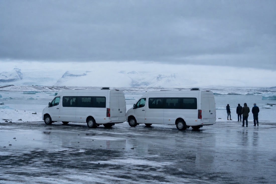 Two identical white minibuses parked side by side on wet snow, plain panels, flat overcast light