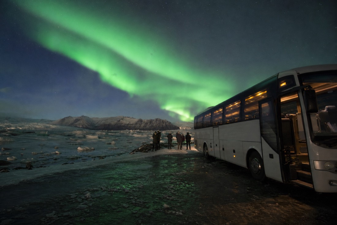An aurora tour bus parked on a dark road under green northern lights outside Reykjavík