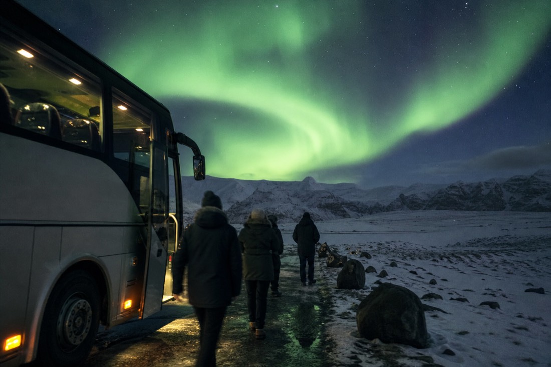 Passengers stepping off a northern lights coach at a dark roadside stop in Iceland