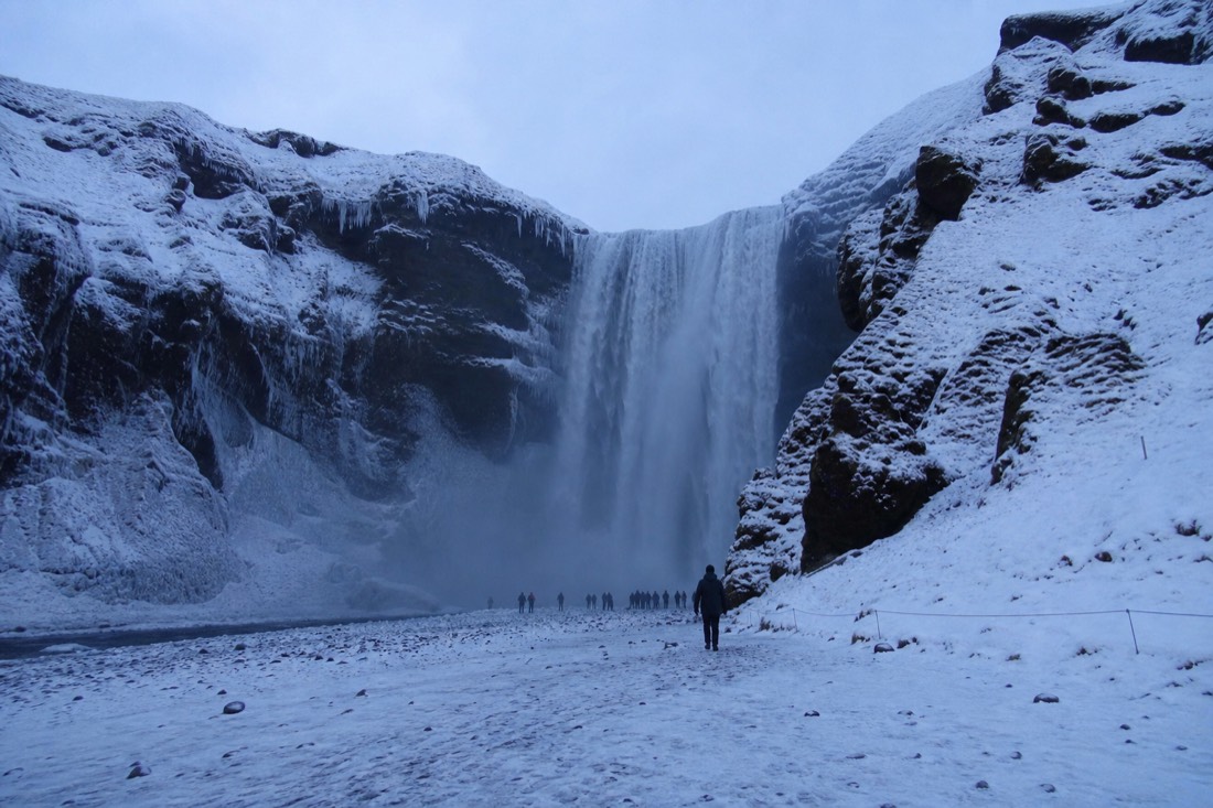Skógafoss waterfall thundering between snowy banks on a South Coast winter day tour