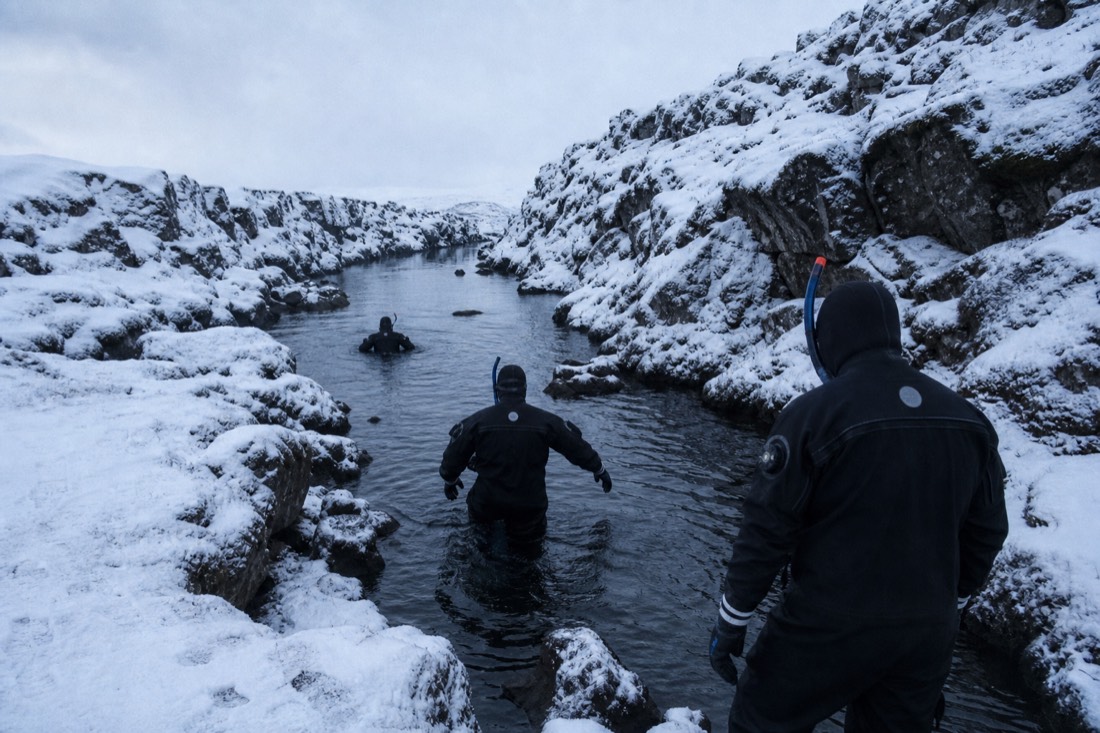 Snorkellers in drysuits entering the Silfra fissure on a winter day at Þingvellir