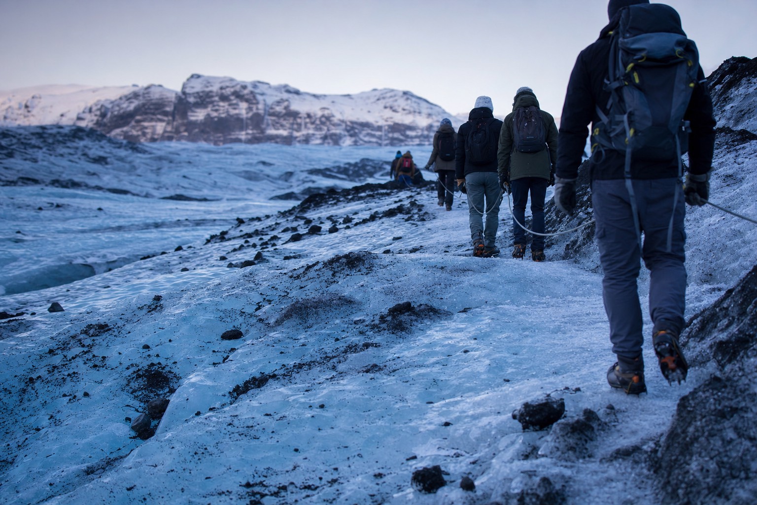 A roped line of hikers in crampons crossing blue ice on a Sólheimajökull glacier hiking tour