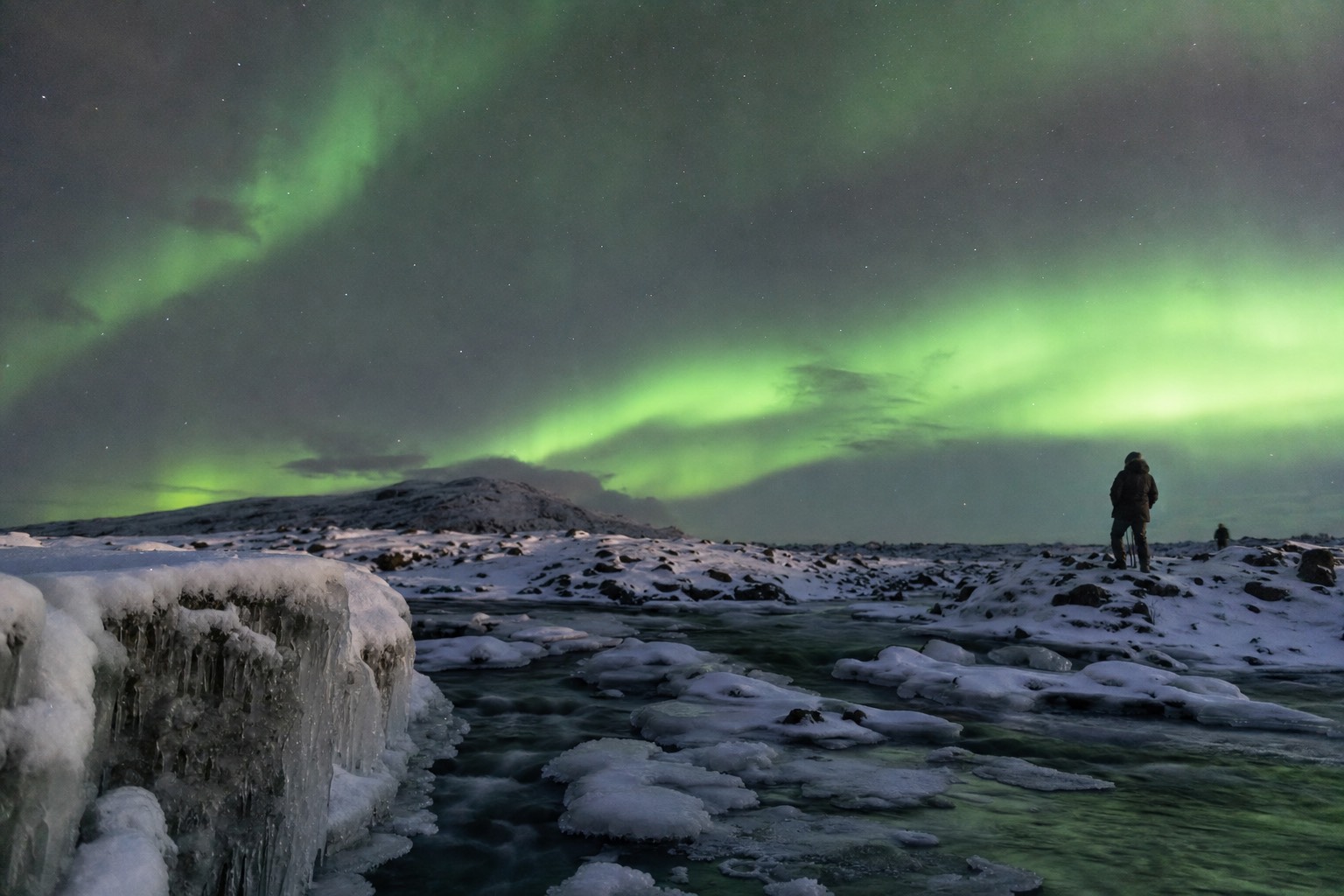 Green northern lights over a snowy Icelandic landscape on a winter aurora tour from Reykjavík