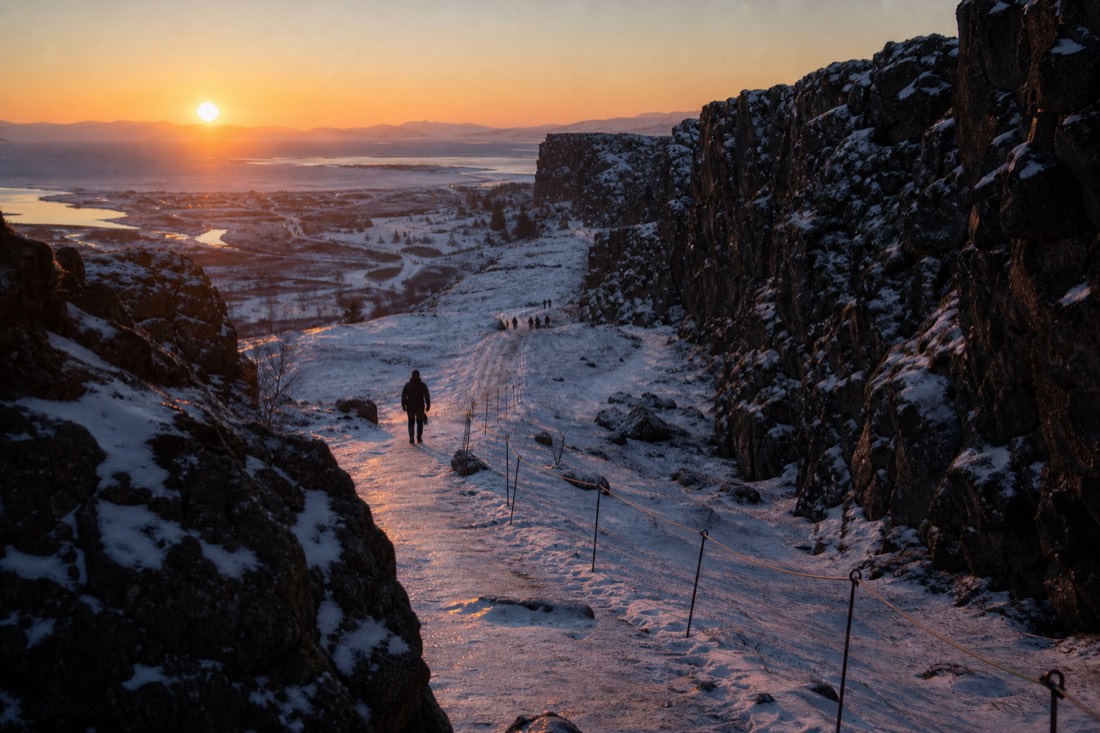 December half-light over Thingvellir, sun low and orange, snow-dusted rift walls in shadow