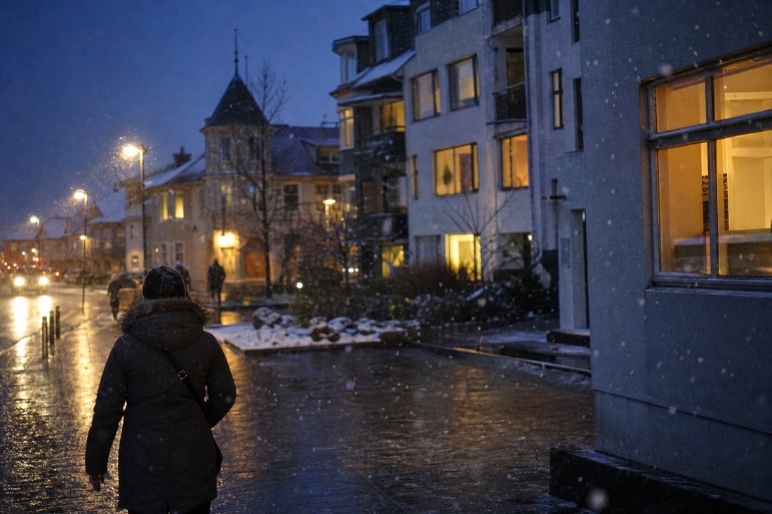 Snow falling on a Reykjavik street at blue hour, warm window light on wet pavement