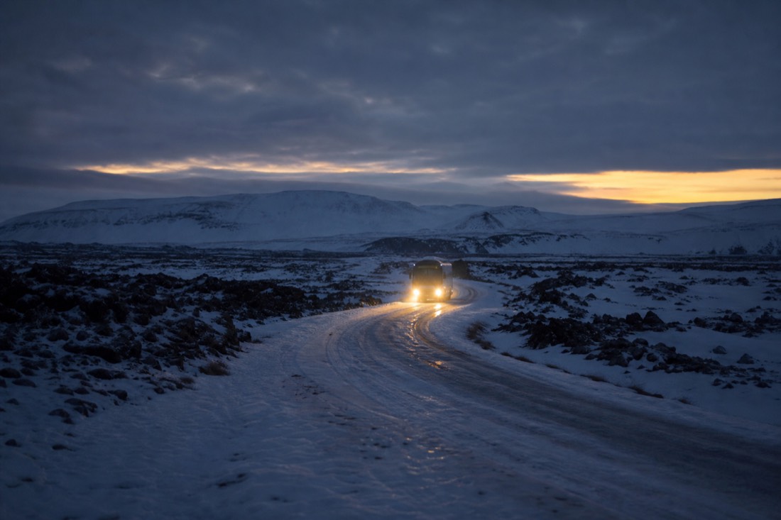 Headlights of a tour coach on a snow-packed Ring Road before dawn, black lava either side
