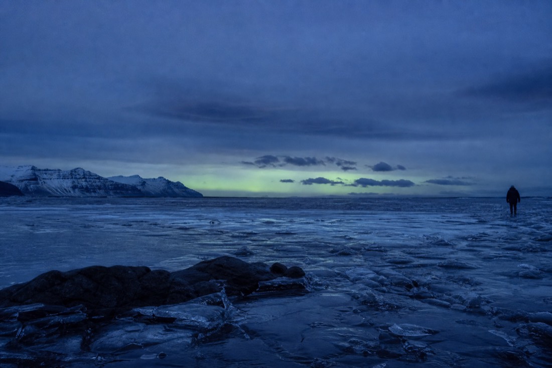 Long winter night over a frozen Icelandic lake, faint green glow low on the northern horizon