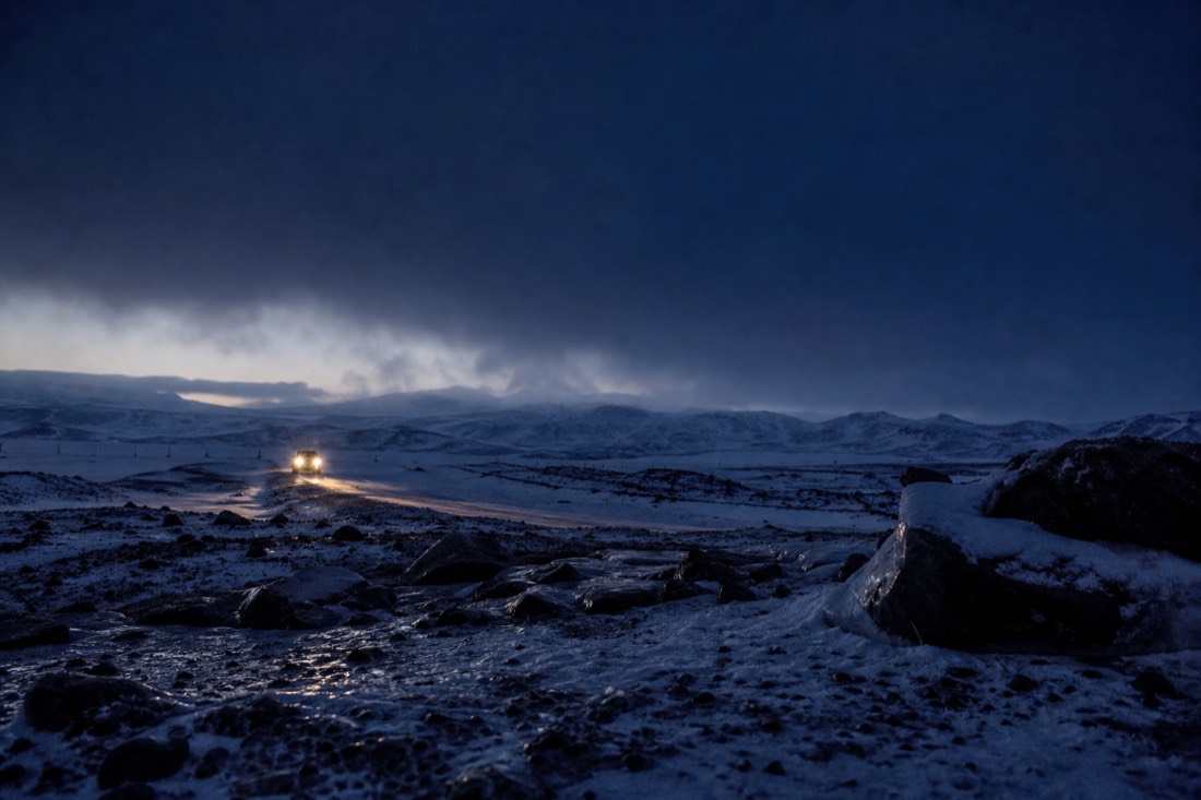 Thick low cloud over a snowy Icelandic plain at night, only headlights breaking the dark