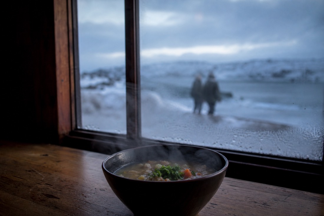 Steaming bowl of soup on a wooden table beside a frosted window in winter daylight