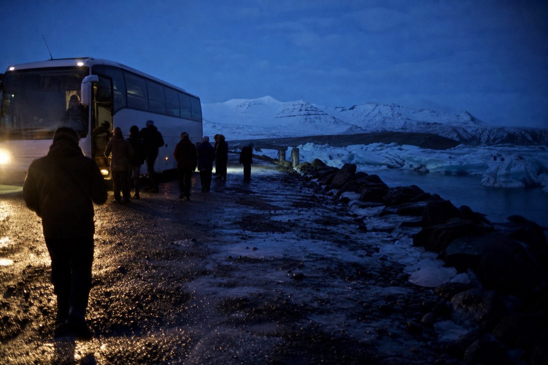 Tour coach loading in darkness at a Reykjavik pickup point, headlights across the snow