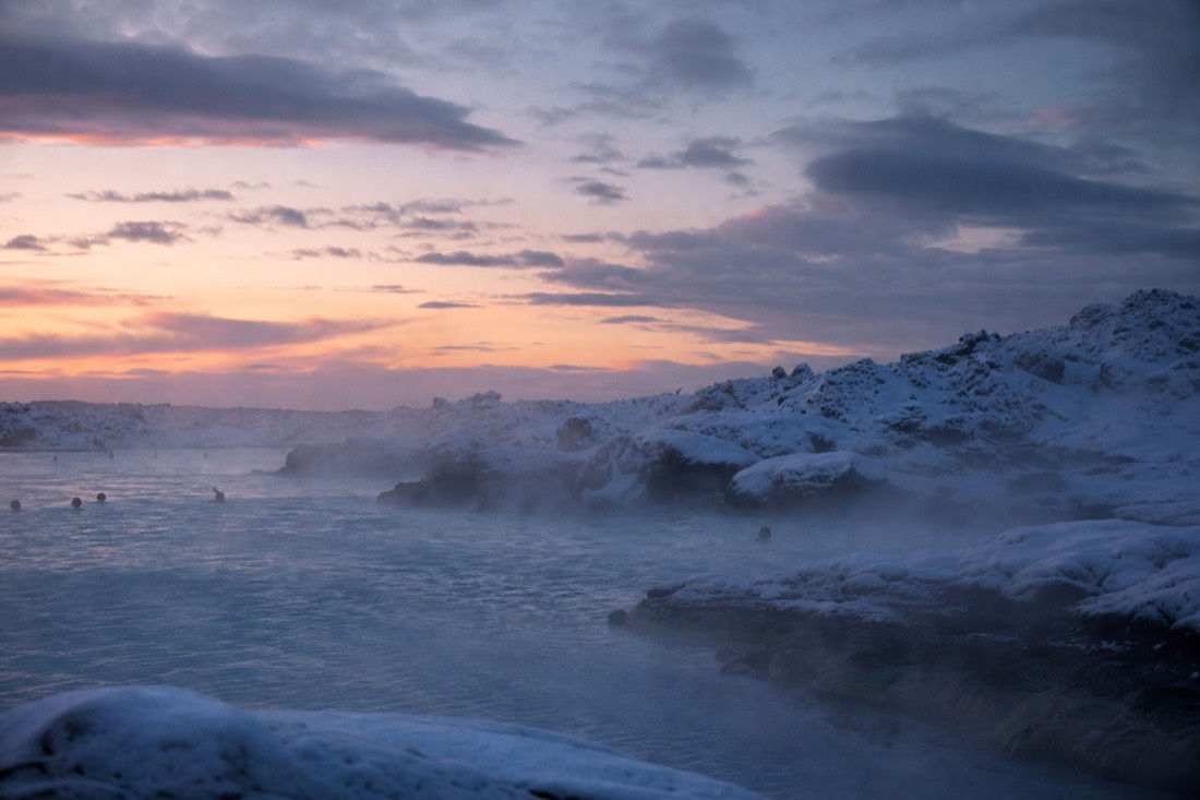 Steam rising off a geothermal lagoon into cold air at dusk, snow along the rim