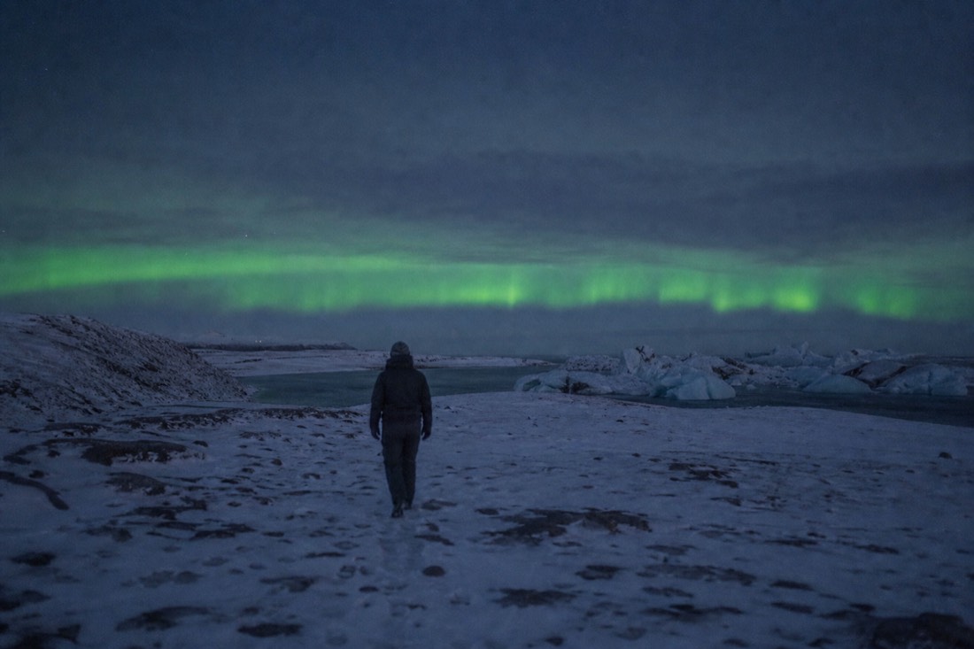 Clear cold night over a snowy Icelandic field, a faint green aurora band low on the horizon