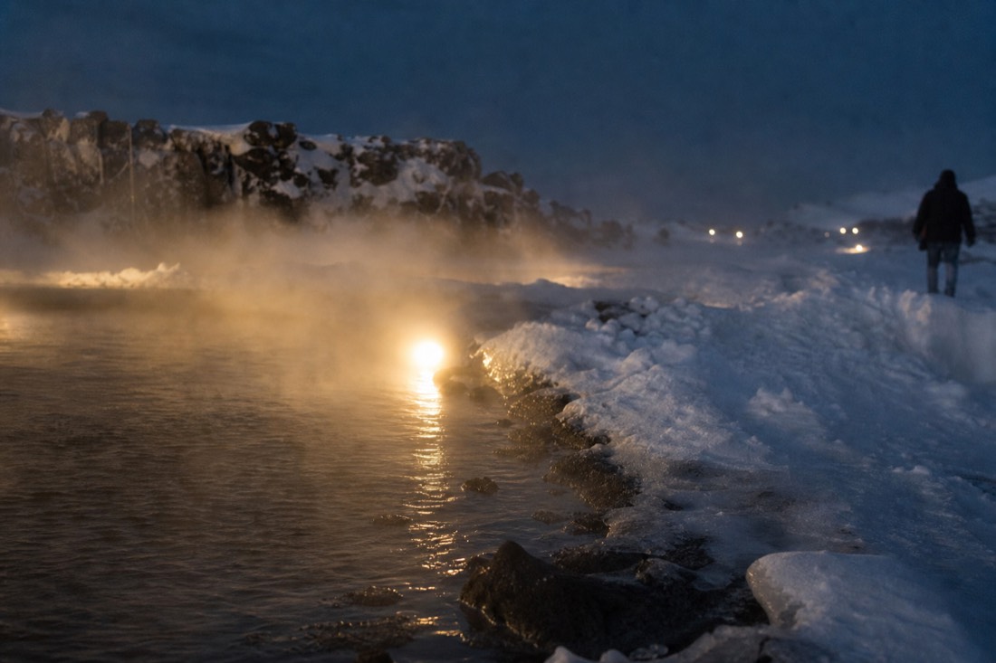 Steam lifting off a lit Icelandic thermal pool after dark, snow banked around the water