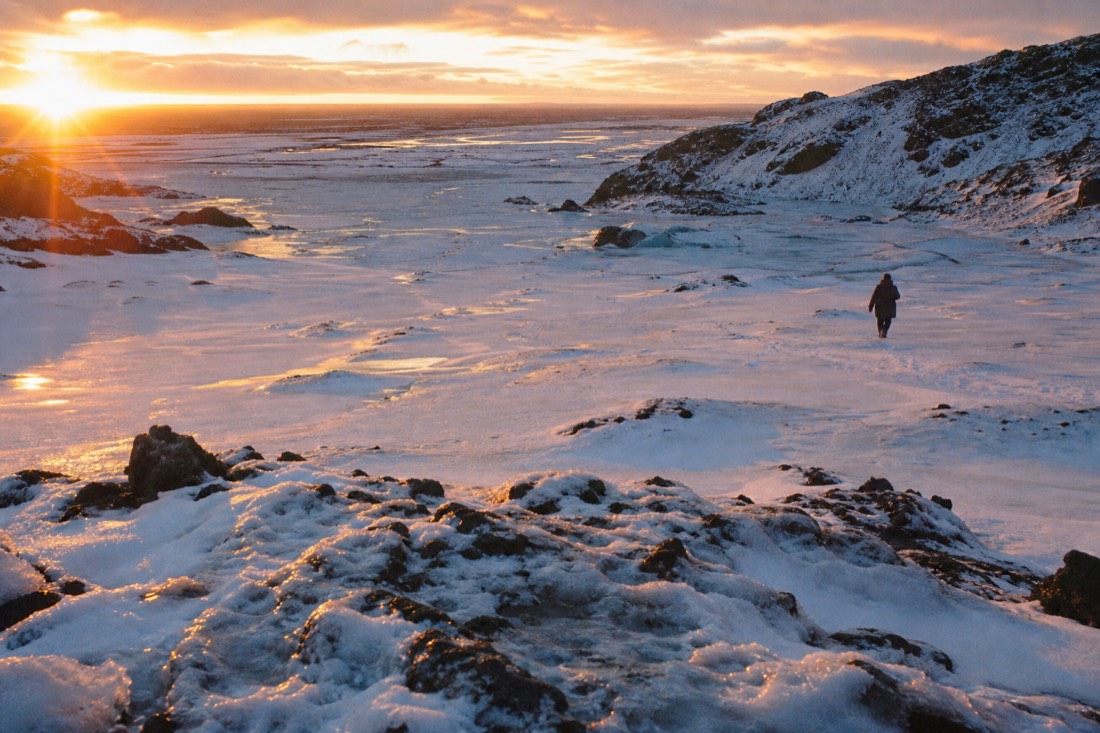 Low December sun scraping the horizon over a snowy lava field, orange light thrown sideways