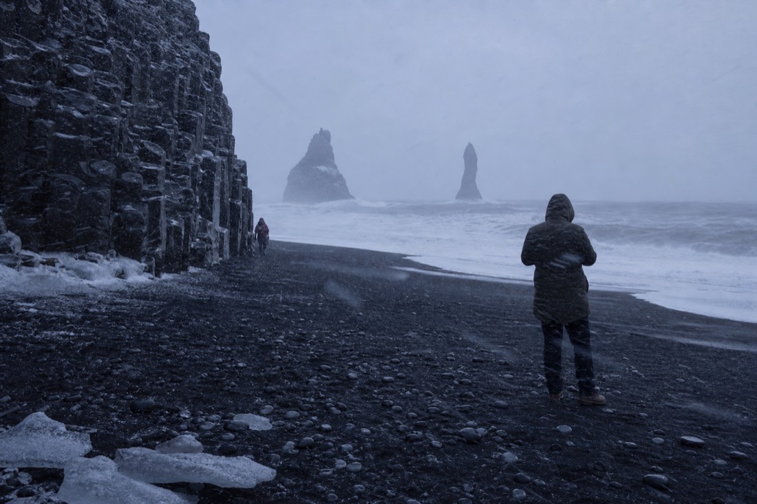 Wind-driven sleet across Reynisfjara black sand in December, dark sea under a grey sky