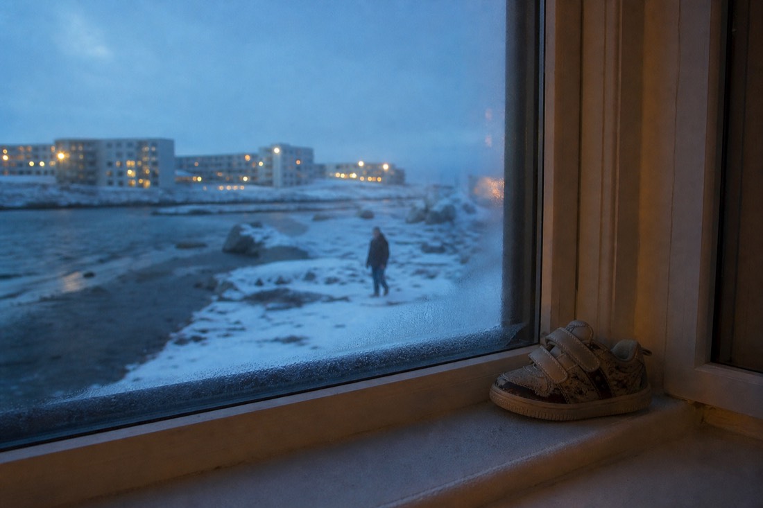 A child's shoe on a frosted windowsill of a lit Icelandic home on a December evening
