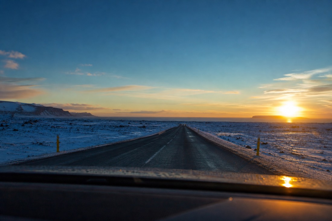 Low February sun through a car windscreen on a cleared road between snowy fields