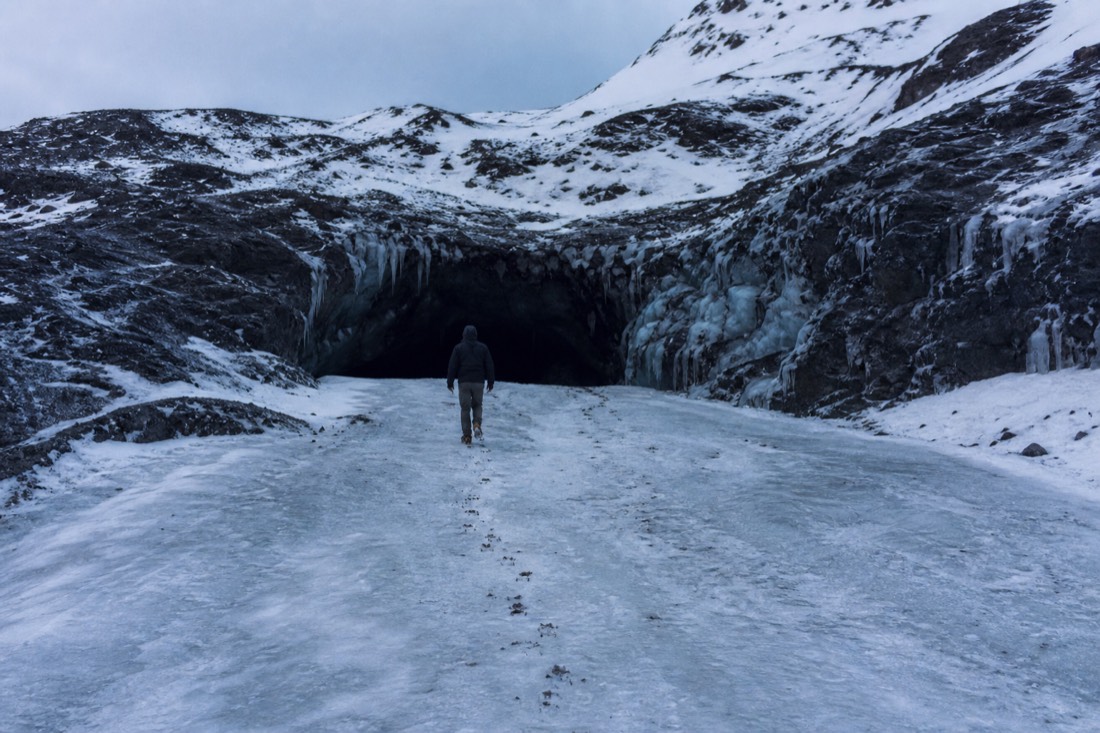 Crampon tracks across swept glacier ice leading to a dark cave mouth in January