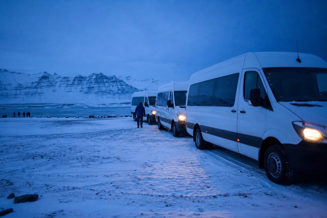 Tour minibuses parked on packed snow outside Reykjavik at blue hour with headlights on